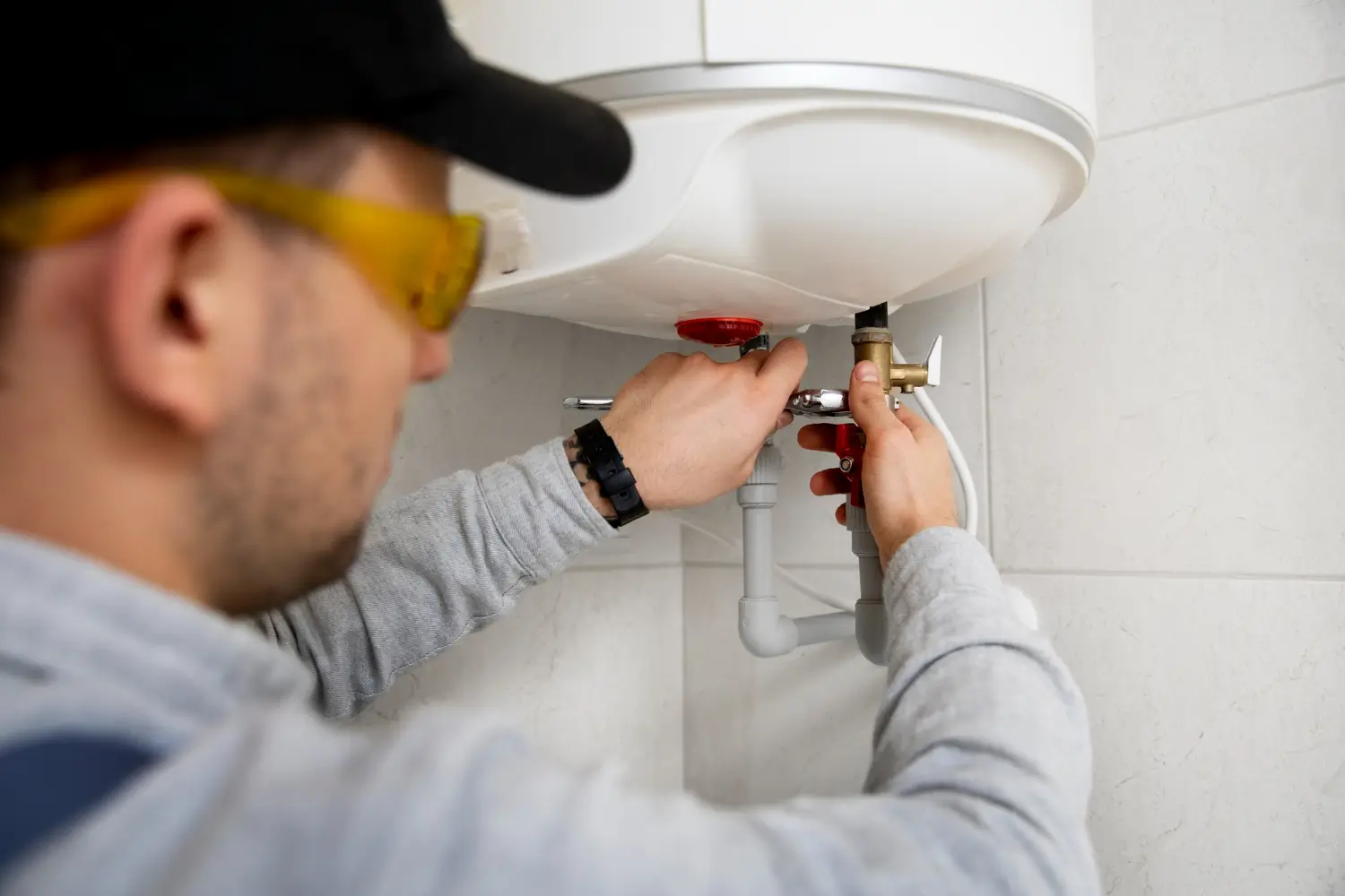Plombier ac-plomberie en haute-garonne réglant un chauffe-eau mural avec clé dans salle de bain carrelée